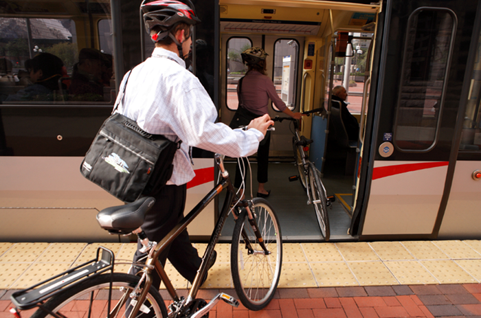 Image of young man getting on public transportation bus with a bicycle.