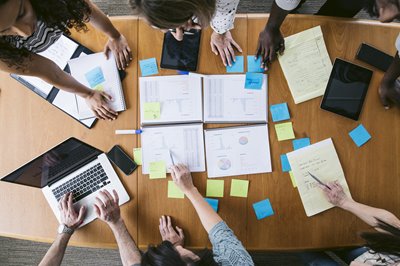 Image of multiple people gathered at a desk with office supplies coordinating a plan